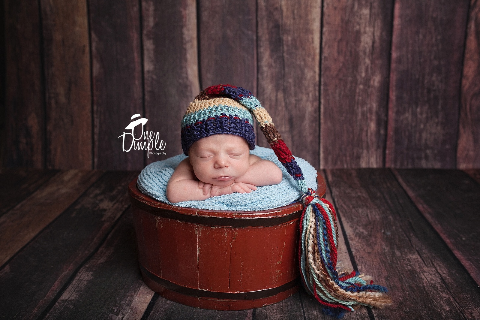 newborn boy in red bucket with wood backdrop