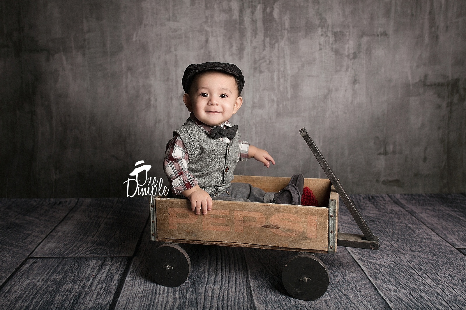 little boy sitting in wooden wagon with drivers hat.