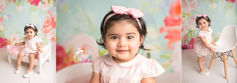 One Dimple Photography is a custom cake smash photographer for Dallas Fort Worth.  1 year portraits of smiling girl in pink dress with floral backdrop
