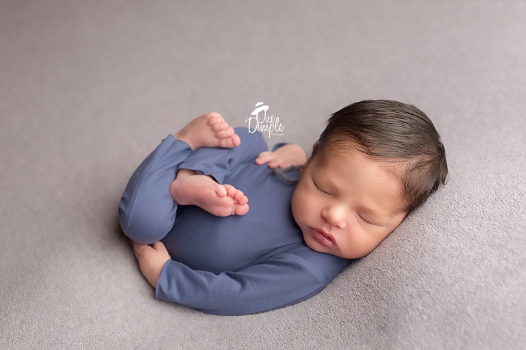 One Dimple Photography is a DFW, Southlake, Trophy Club, Grapevine, Keller newborn photographer. In-Home Newborn Session with baby in blue romper in back laying pose