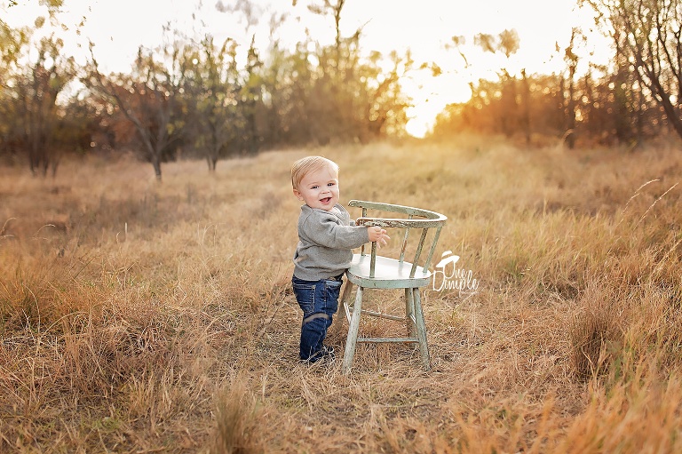One Dimple Photography is a Dallas Fort Worth Baby and Family photographer.  Outdoor family and 6 month milestone session in Southlake, TX. Baby holding on to chair smiling